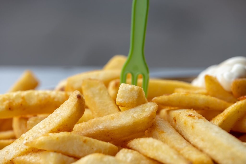 Close-up of golden fries with a green plastic fork and a dollop of white sauce in the background, showcasing a delicious snack perfect for your next Cority break.