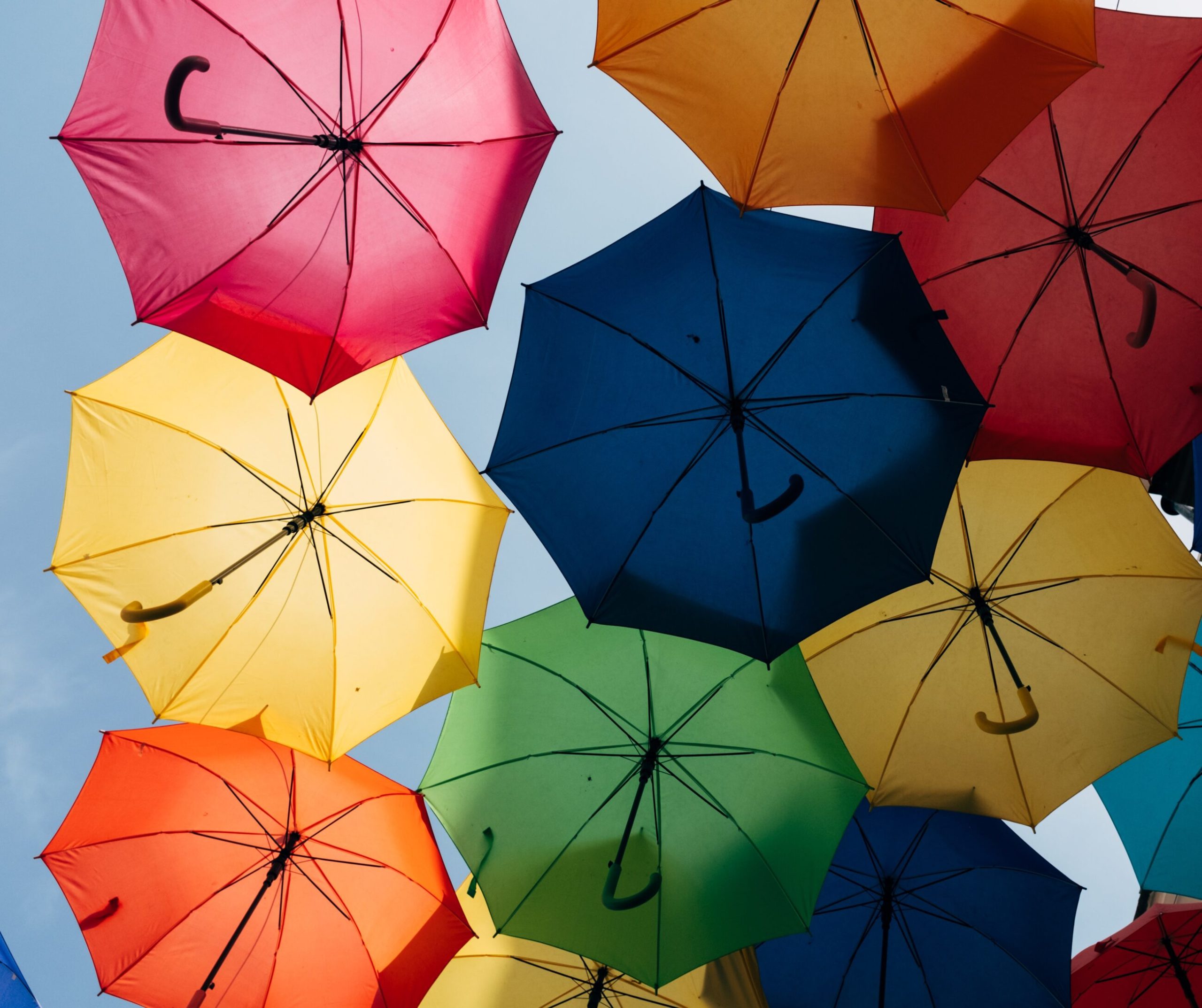 Colorful umbrellas seen from below, overlapping against a blue sky, evoke a sense of unity—much like ESG & sustainability coming together to create a brighter future.