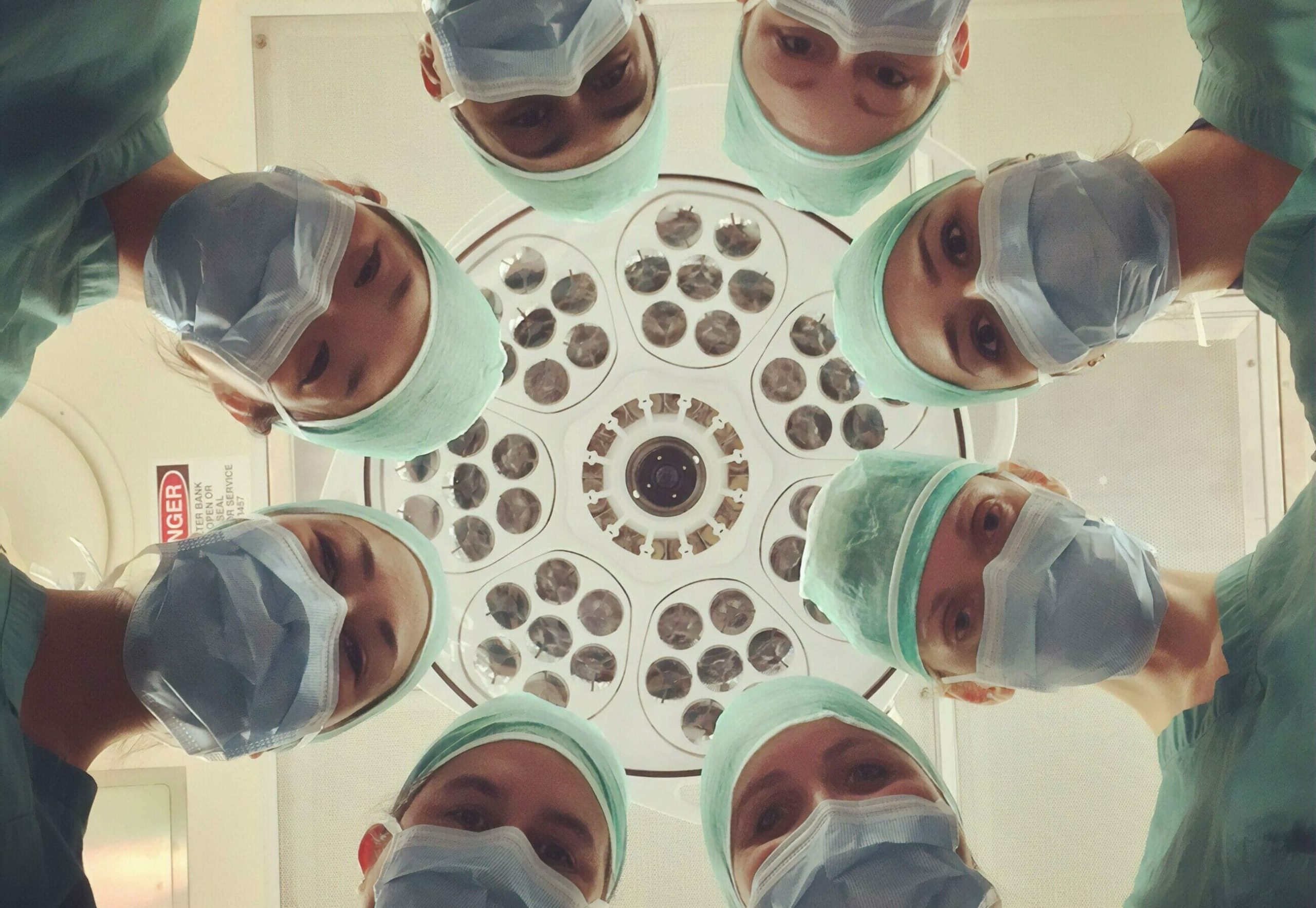 Six surgeons in scrubs and masks look down under a bright surgical light in an operating room, embodying the commitment to ESG in Healthcare through responsible and ethical medical practices.