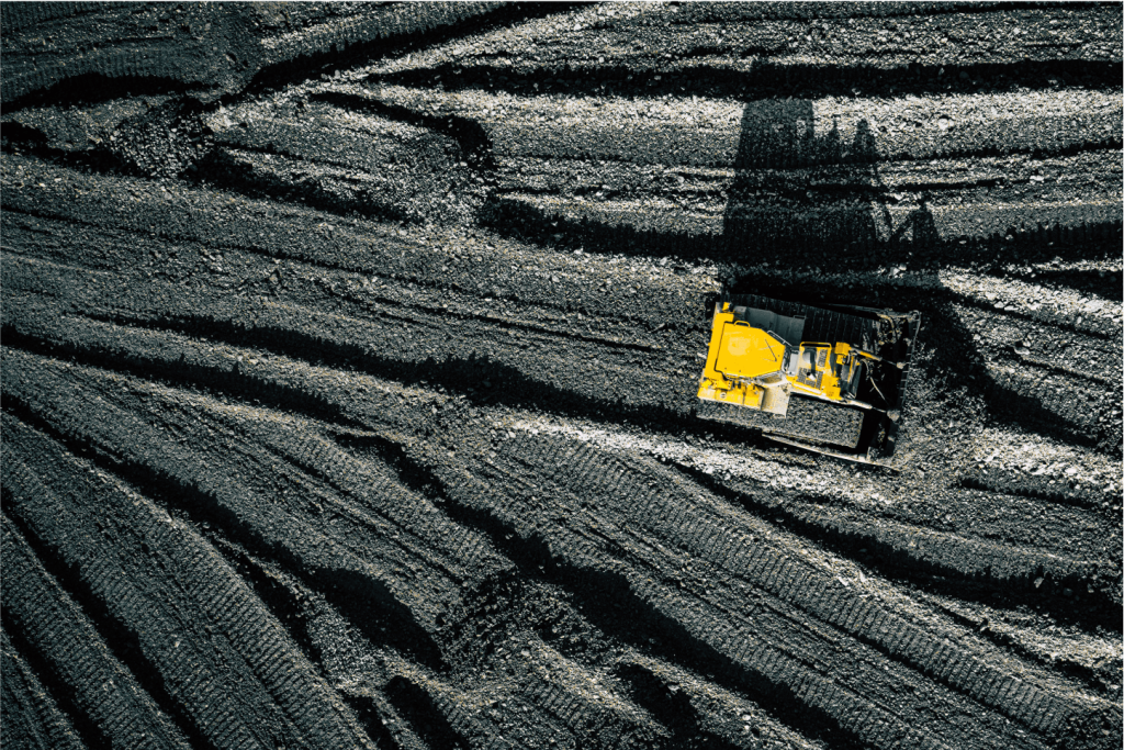A yellow bulldozer moves across dark, textured, striped earth from an aerial perspective, highlighting the importance of safety in construction for World Safety Day.