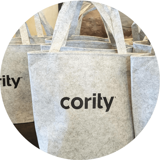 A close-up of several light gray felt tote bags, with "cority" printed in black on the front, standing upright and overlapping—highlighting Sustainability at Cority through eco-friendly design.