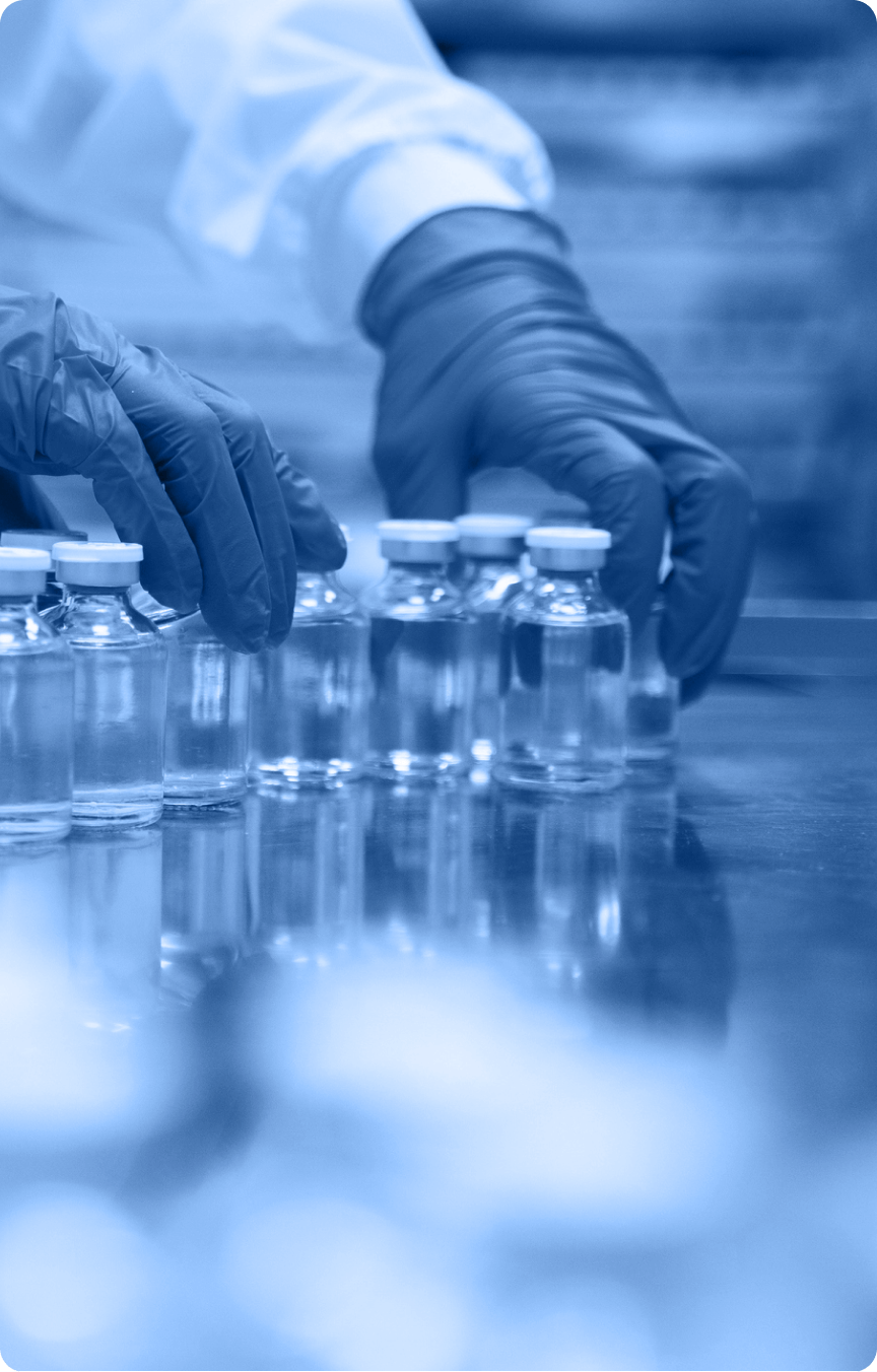 A person wearing dark gloves arranges small glass vials with clear liquid on a reflective surface in a laboratory setting, showcasing the precision and care found across the industry.