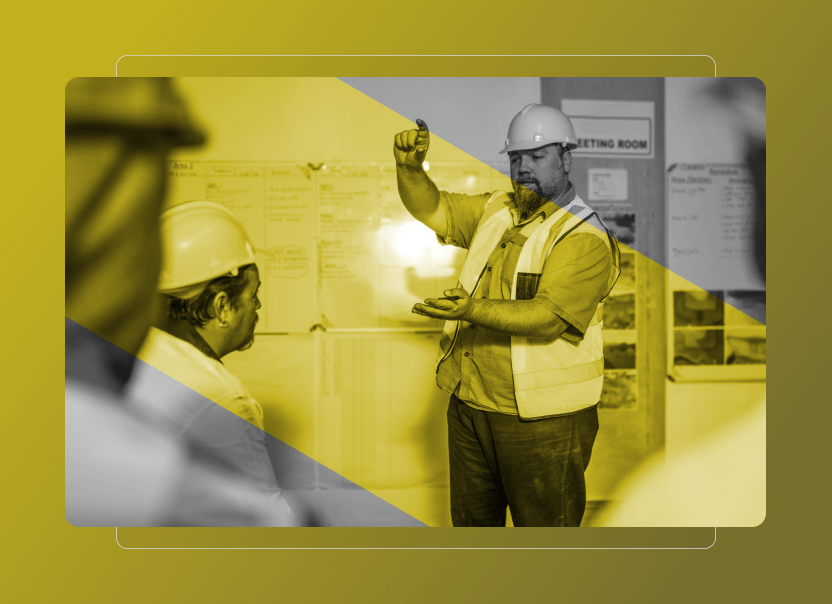 A construction worker in a hard hat and safety vest discusses Safety Cloud features while holding up a small object in a meeting room with charts on the wall. The image has a yellow overlay with diagonal stripes.