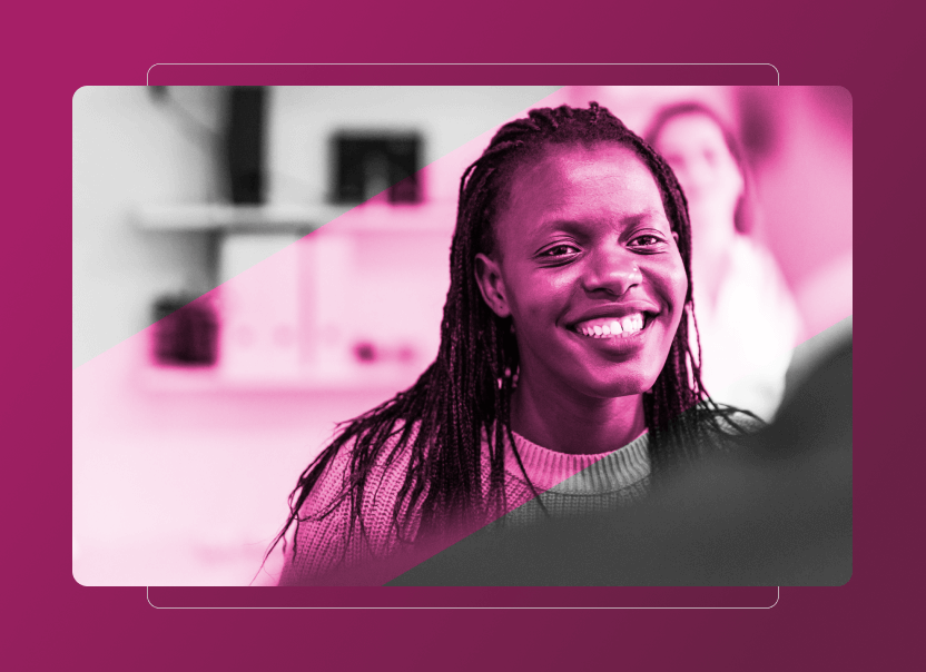 A woman with braided hair smiles warmly at someone off-camera. The image, tinted pink, features a blurred background and another person in soft focus—perfect for illustrating an Accordion Section on sustainability or the benefits of Sustainability Cloud.